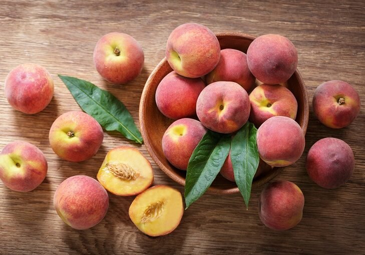 Fresh ripe peaches in a bowl on a wooden table, top view